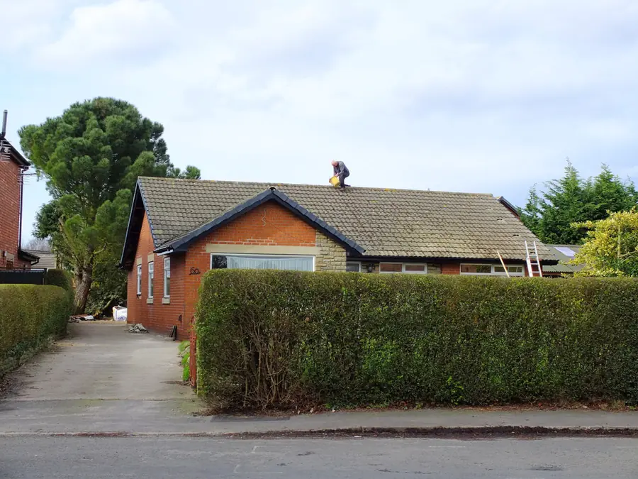 Roofer on the ridge of a tiled bungalow roof repairing ridge tiles