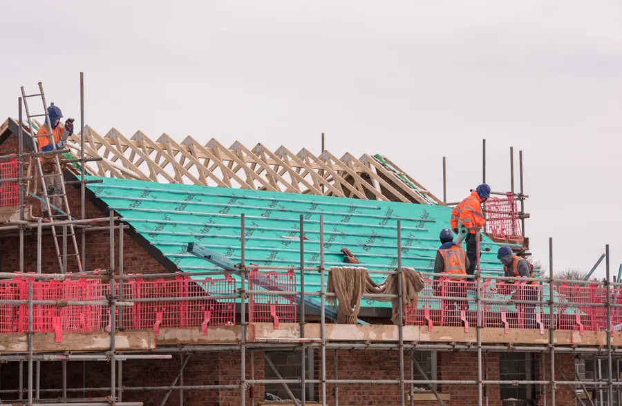 Roofers in hi-vis fixing breathable membrane over new roof trusses from scaffolding