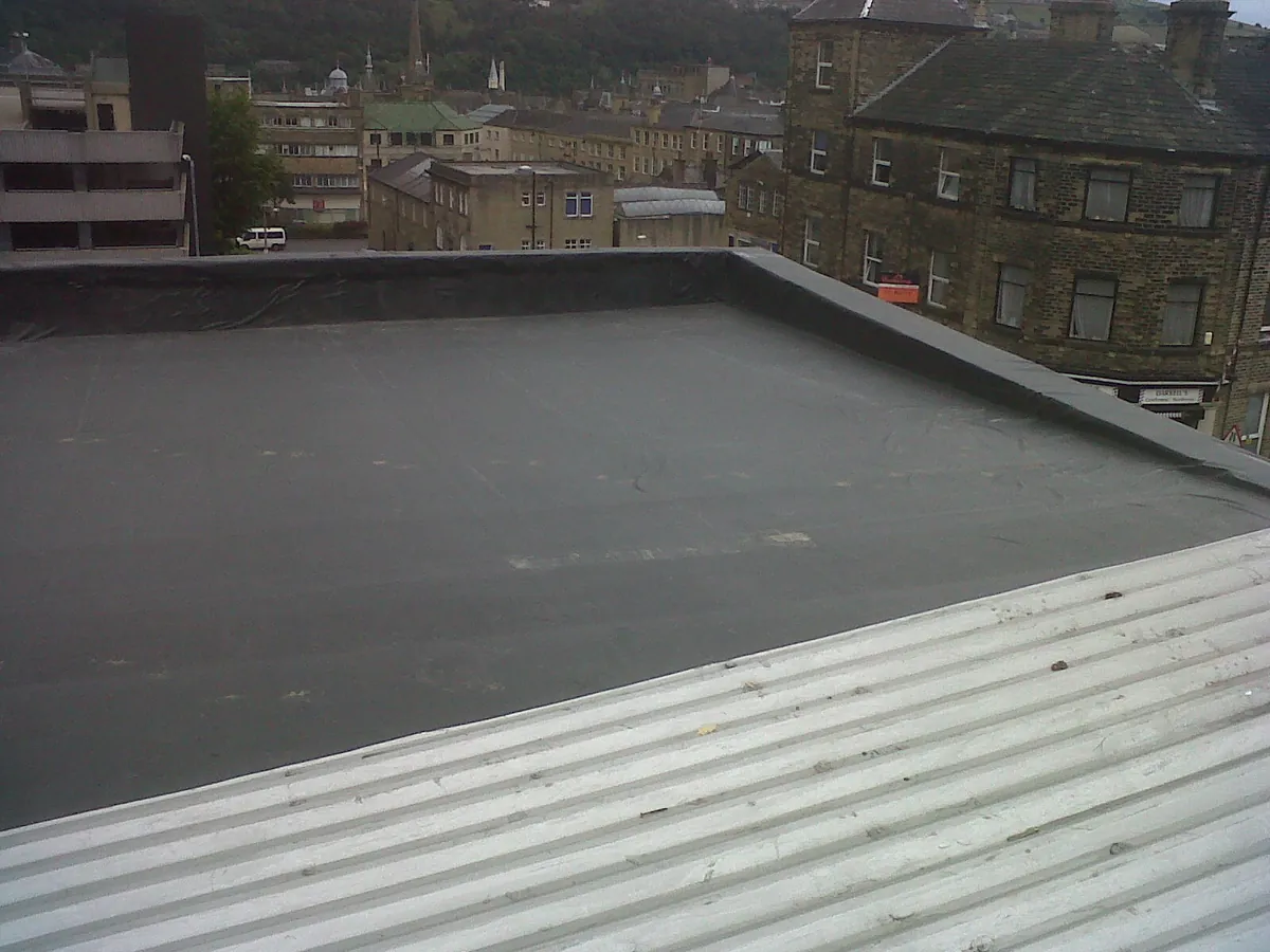 Newly laid EPDM rubber flat roof with trimmed edges beside stone-built town buildings