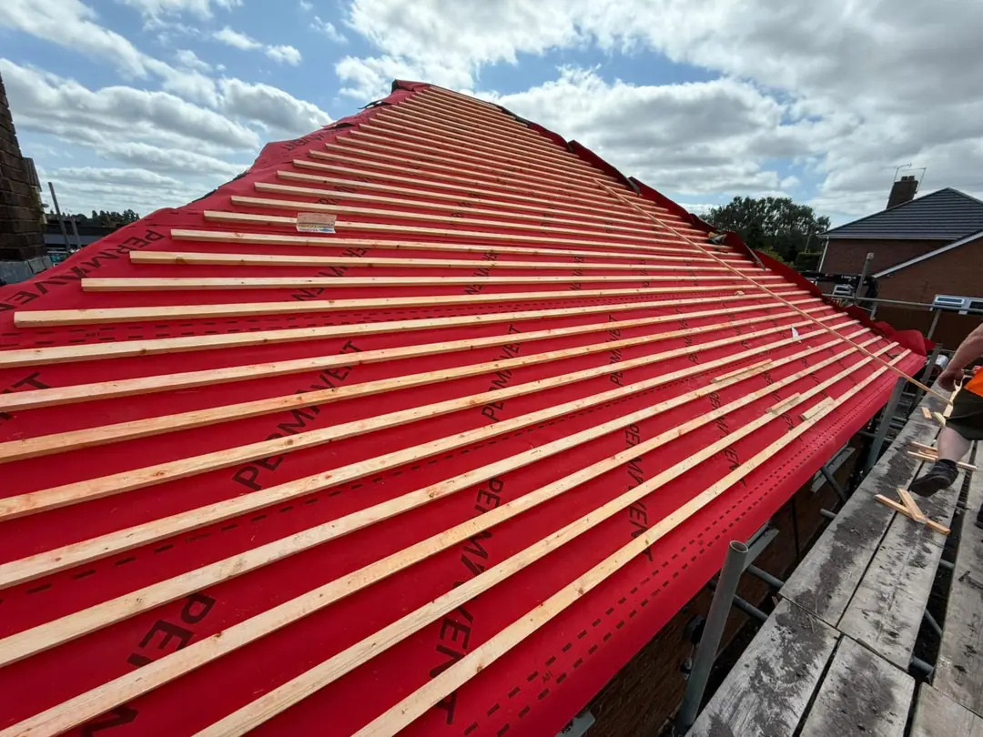 New roof under construction with red breathable membrane and fresh treated battens fixed ready for tiling