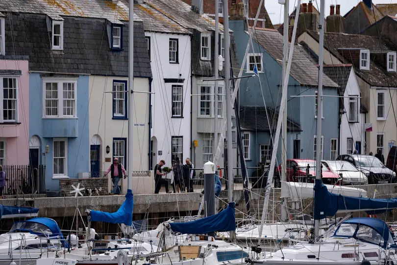 Pastel harbourside terraces with weathered slate roofs, dormers and chimneys behind moored yachts in a Dorset seaside town